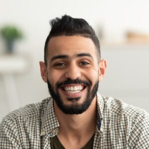 portrait of handsome young arab man smiling and looking at camera sitting on sofa at home e1687402178567 akademi kakao